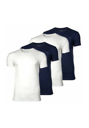 Młody mężczyzna stoi, ubrany w granatowy t-shirt z krótkim rękawem i jasnoszare spodnie na jednolitym jasnoszarym tle.