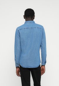 Hellblaues Jeanshemd mit langen Ärmeln, spitzem Kragen und geknöpften Manschetten. Verfügt über einen geraden Schnitt und ein Rückenpasse-Design.
