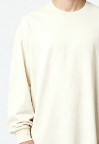 Gros plan d'une personne portant un t-shirt uni à manches longues, blanc cassé, avec des poignets côtelés.