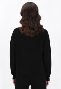 Czarny, oversize sweter z mi�ękkiej dzianiny, o luźnym kroju, z opadającymi ramionami i ściągaczami. Gładka faktura, minimalne detale.