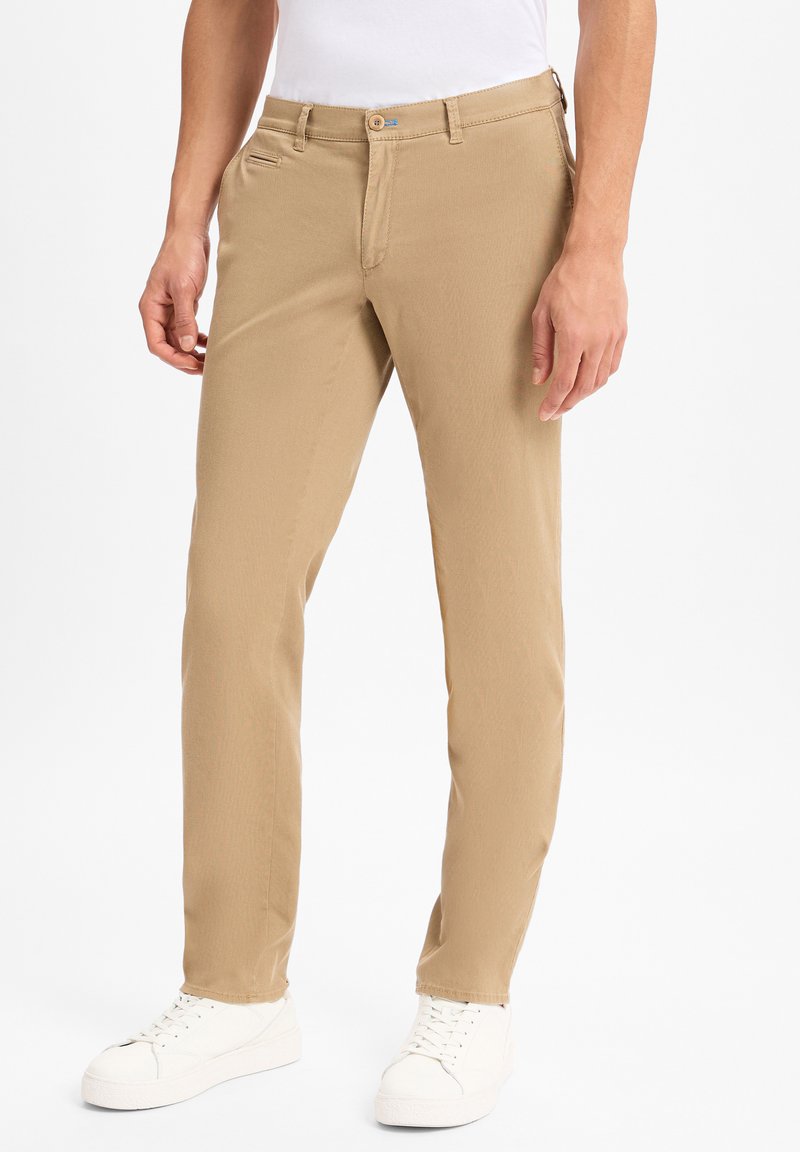 Chino beige en coton, présentant une coupe droite, des poches avant et une fermeture à un bouton. Associé à des baskets blanches.