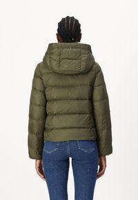 Giacca puffer verde oliva con cappuccio, caratterizzata da un design trapuntato e polsini elasticizzati. Abbinata a jeans blu, con una vestibilità comoda.