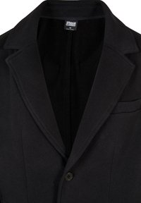 Svart blazer med slagkrage, enkel knappstängning och en ficka. Tillverkad av slät tyg, med ett mesh-foder inuti.