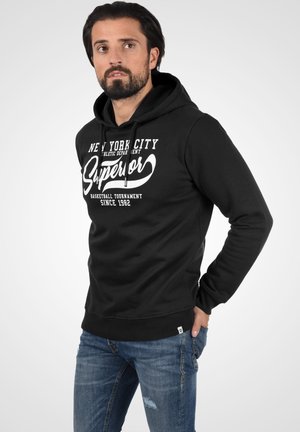 Sudadera con capucha negra con el texto blanco "New York City Superior" y un diseño de baloncesto. Cuenta con un bolsillo tipo canguro en la parte frontal y puños acanalados.
