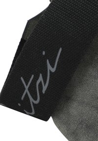 Cintura in tessuto nero con una superficie testurizzata, dotata di un logo grigio distintivo. Lo sfondo è in un materiale grigio liscio.