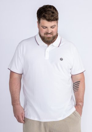 Polo bianco con una patta a due bottoni, rifiniture blu navy e rosse sul colletto e sulle maniche, con un piccolo logo sul petto.