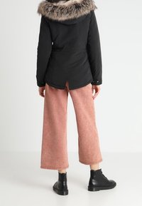 Svart jacka med pälsfodrad huva, matchad med ljusrosa vida byxor och svarta snörstövlar. Texturerade material synliga.