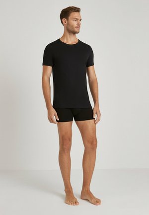 Zwarte t-shirt met korte mouwen en een ronde hals, gecombineerd met zwarte boxershorts. De stof lijkt glad en heeft een aansluitend ontwerp.