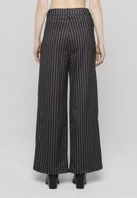 Czarne spodnie o szerokich nogawkach w prążki, z wysokim stanem, charakteryzujące się gładką fakturą i kieszeniami. Wykończone prostym, czystym designem.