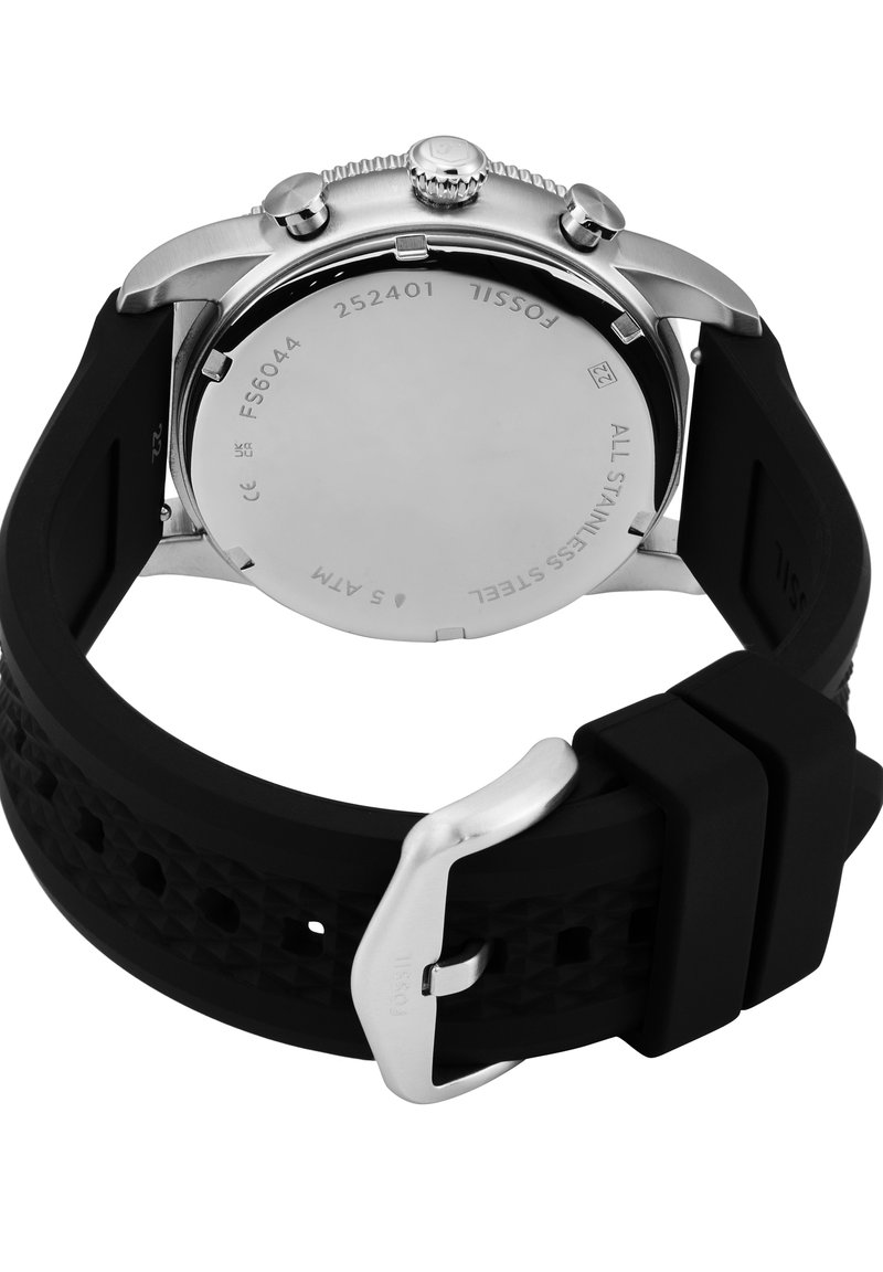 Parte trasera del reloj Fossil de acero inoxidable con correa de silicona negra texturizada y hebilla plateada, mostrando el número de modelo FS6044 y resistencia al agua de 5 ATM.