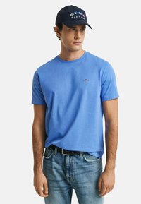T-shirt in cotone blu chiaro con colletto rotondo e maniche corte. Indossato con jeans in denim chiaro, con una cintura nera e un cappellino blu navy con loghi.