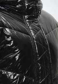 Gros plan d'une doudoune noire brillante matelassée avec un col montant et des détails de couture visibles à l'avant et aux épaules.