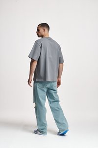 Mees seisab külgsuunas, kandes lahtisi helesiniseid rebenditega teksaseid, halli ülikoopsu t-särki ja sinise-valgeid tossusid.