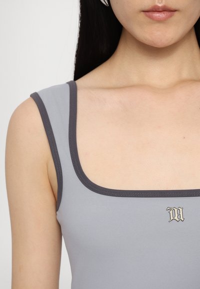Grå tanktop med firkantet udskæring og mørkegrå kant, prydet med et lille logo i guld i midten. Glat, strækbart materiale.