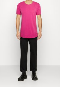 T-shirt fucsia a maniche corte con collo tondo, realizzato in cotone, con un piccolo logo sul petto, abbinato a pantaloni neri con risvolto.