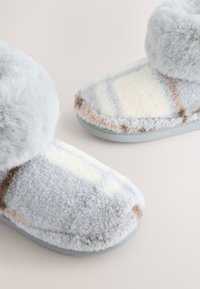 Grau-cremefarbene, flauschige Hausschuhe mit weicher, plüschiger Textur, ausgestattet mit einem gemütlichen Oberteil und dezenten Musterakzenten. Abgerundete Form mit Gummisohlen.