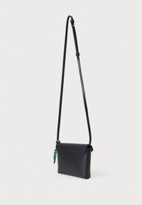 Černá kožená crossbody taška s moderním designem, která obsahuje zelenou šálku uvázanou na popruhu a nastavitelné ramenní popruhy.