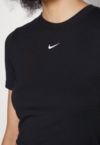 Svart bomull T-shirt med korta ärmar, med en liten vit Nike-logotyp på bröstet, rund halsringning och en slät textur.