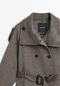 Cappotto grigio doppiopetto in lana con grandi bottoni neri, vita con cintura e ampio colletto. Dotato di spalline e texture liscia.