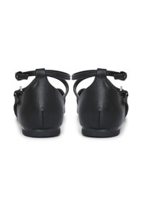 Sandalias planas de cuero negro con tiras alrededor del tobillo, mostradas desde atrás sobre un fondo blanco.