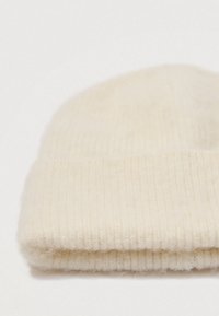 Foldet cremefarvet ribbet strikhue på en hvid baggrund.