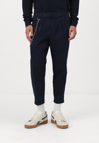 Námořnicky modré chino kalhoty s záhyby, zdobené kovovým řetízkem na pase. Kombinované s krémovými teniskami a bílými ponožkami.