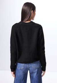 Svart, ribbad stickad tröja med rundad halsringning och långa ärmar; matchad med ljusblå denimjeans. Texturen är tjock och mysig.