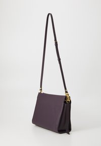 Purple leather crossbody bag with a long adjustable strap and gold hardware accents. Smooth texture and minimalist design.