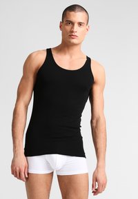 Schwarzes Baumwoll-Tanktop mit rundem Ausschnitt und breiten Schulterträgern, kombiniert mit weißer Unterwäsche. Glatte Textur, figurbetontes Design.