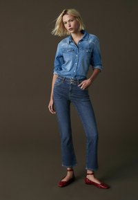 Jeansskjorta med två bröstfickor och broderidetaljer; kombinerad med högmidjade raka jeans; röda ballerinas med vita accenter.