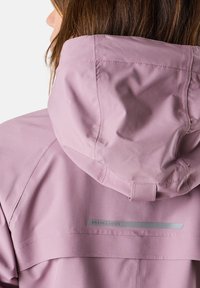 Rosa vattentät jacka med en figursydd huva, slät textur, reflekterande logotypdetalj och synlig sömnad längs sömmarna.