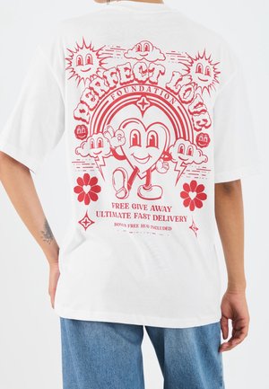 T-shirt en coton blanc avec un motif graphique rouge comprenant des cœurs souriants, des nuages et du texte. Manches courtes et coupe décontractée.
