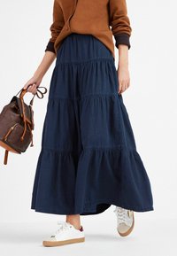 Gonna maxi a strati blu navy realizzata in tessuto morbido, con cuciture arricciate. Abbinata a sneaker bianche e una borsa marrone.