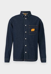 Dark blue denim shirt with button-down collar, orange label on chest pocket, and white buttons. Soft texture with contrast stitching details.