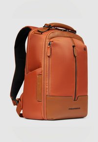 Zaino arancione con texture, dettagli in pelle, scomparti con cerniere multiple, spallacci imbottiti e manico superiore per opzioni di trasporto versatili.