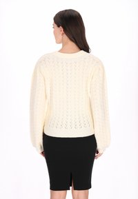 Kremowy sweter z dzianiny w zygzakowaty wzór, z prążkowanymi mankietami i okrągłym dekoltem, zestawiony z czarną spódnicą ołówkową z rozcięciem z tyłu.