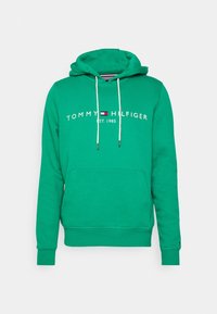 Felpa verde Tommy Hilfiger con lacci bianchi, tasca frontale e testo del logo "TOMMY HILFIGER EST. 1985" sul petto.