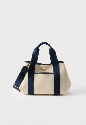 Beige stofhåndtaske med marineblå håndtag, justerbar skulderrem, forlommer og lukning med guldknap.