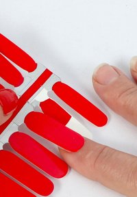 Display van rode nagellakstalen met meerdere tinten rood, met glanzende en matte afwerkingen, naast een hand met geschilderde nagels.