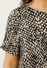 Nahaufnahme einer kurzärmeligen Bluse aus beige und schwarzem tierischen Druck mit Struktur auf dem Oberarm und der Schulter einer Person.
