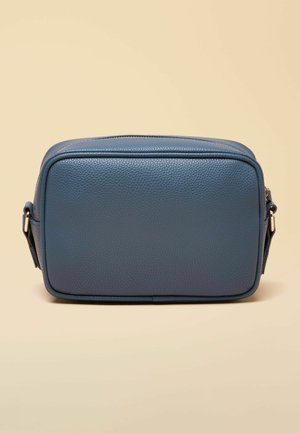 Rechteckige blaue Leder-Umhängetasche mit genarbter Textur, goldfarbenem Reißverschluss und verstellbarem Schulterriemen vor beigem Hintergrund.