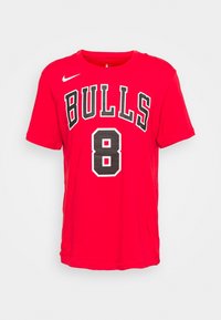 T-shirt rossa in cotone con la scritta "BULLS" in bianco e nero, e il numero "8" su un patch nero testurizzato. Collo a giro e maniche corte.