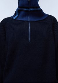 Granatowy sweter z dzianiny z wysokim kołnierzem na zamek i kontrastującymi niebieskimi paskami w okolicy szyi. Teksturowana tkanina.