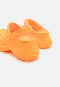 Orange Crocs klipklappere med en tekstureret overflade, bagsnøring og ventilationshuller. Tykk, polstret sål for komfort.