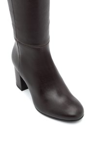 Bota alta de cuero marrón con punta afilada, tacón cuadrado y detalles de costura mínimos en el eje. Textura suave y diseño elegante.