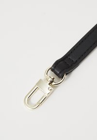Bracelet en cuir noir avec un fermoir et des accessoires en métal doré brillant, présentant des bords cousus et une texture lisse.