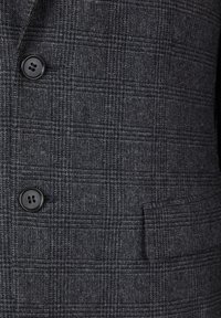 Šedý kostkovaný blazer s texturovanou tkaninou, dvěma černými knoflíky a boční kapsou. Vzor obsahuje jemné světlé a tmavé kontrasty.
