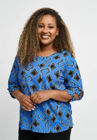 Zila rakstainā blūze ar ģeometrisku dizainu melnā un pelēkā krāsā. Trīs ceturtdaļu piedurknes ar saišu detaļām un brīvu piegriezumu.