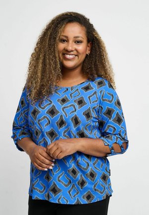 Zila rakstainā blūze ar ģeometrisku dizainu melnā un pelēkā krāsā. Trīs ceturtdaļu piedurknes ar saišu detaļām un brīvu piegriezumu.