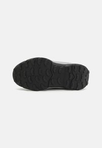 Black rubber shoe sole with deep treads, textured surface, and angular patterns for grip and traction. Slightly raised heel section.